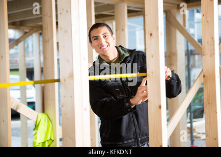 Young Carpenter Measuring Wood At Construction Site Stock Photo