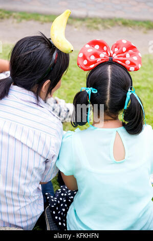 Two young Thai girls hang out in Bangkok on a sunday with elaborate head gear. Stock Photo