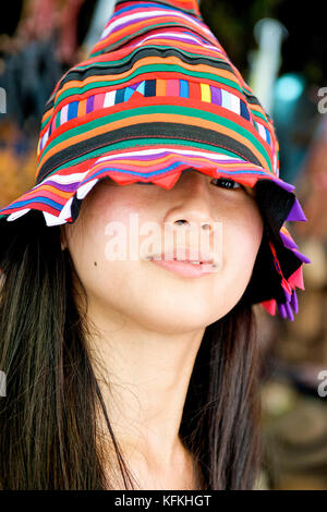 A young Asian girl shows her traditional Thai hat off at the famous Bangkok weekend market called Chatuchak market. Stock Photo