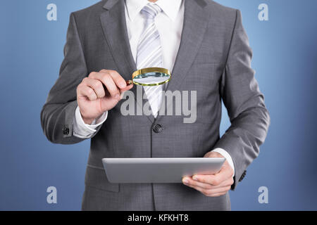 Auditor holding magnifying glass and tablet. Over blue background Stock Photo