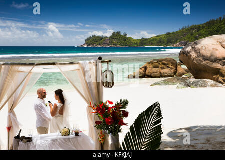 The Seychelles, Mahe, Baie Lazare, beach, wedding couple exchanging vows from words on phone Stock Photo