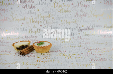 Christmas food photography image of mince pie pies with cinnamon sticks spice on xmas wrapping paper in white gold with seasonal writing words Stock Photo