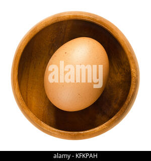 Whole chicken egg in wooden bowl. Raw slightly speckled brown egg from a hen. Common food and versatile ingredient used in cooking. Photo. Stock Photo