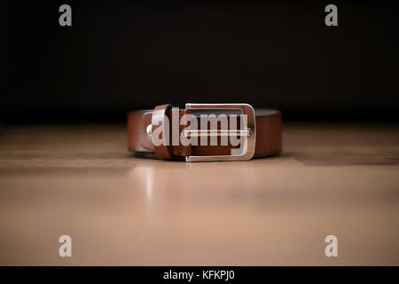 Isolated business brown leather male belt with visible silver buckle set on a brown table with dark background Stock Photo