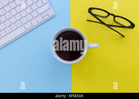 Computer keyboard and coffee cup overhead on bright blue and yellow background Stock Photo