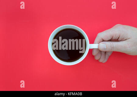 Hand holding coffee cup overhead on bright red background Stock Photo