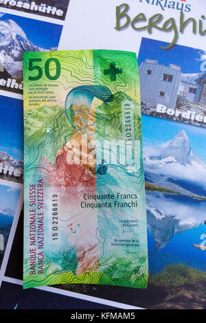 ST. NIKLAUS, SWITZERLAND - Swiss franc note with image of paraglider, 50 CHF, in front of tourism guide. Stock Photo