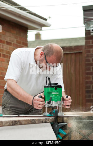 Man cutting kitchen unit top outside residential property using a wood router. Stock Photo