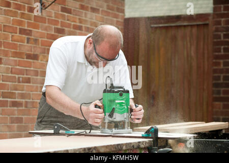 Man cutting kitchen unit top outside residential property using a wood router. Stock Photo