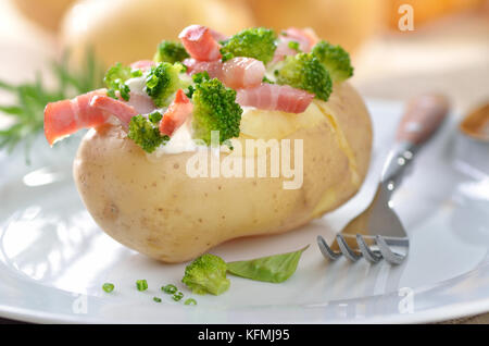 Baked potato stuffed with fried bacon strips, broccoli, chives and creme fraiche Stock Photo