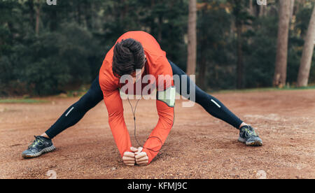 Runner doing stretching exercises in a park listening to music. Man wearing earphones warming up before a run. Stock Photo