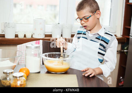 7-year-old boy mixing ingredients for baking a cake. Lifestyle image of son helping in the kitchen. Stock Photo