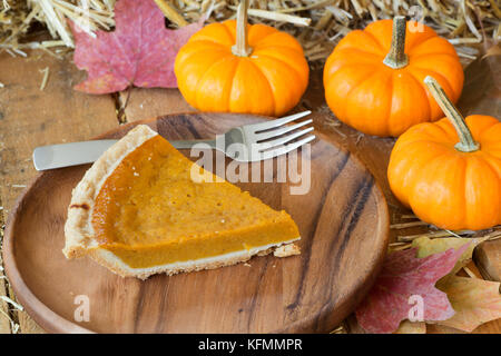 Slce of pumpkin pie on a wooden plate with pumpkins Stock Photo