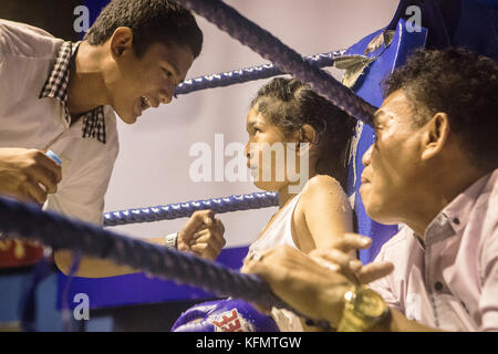 Hasana, 7 years old and 7 matches, muay Thai fighter sitting in the conner of the ring, advised by his coaches, between rounds, Bangkok, Thailand Stock Photo