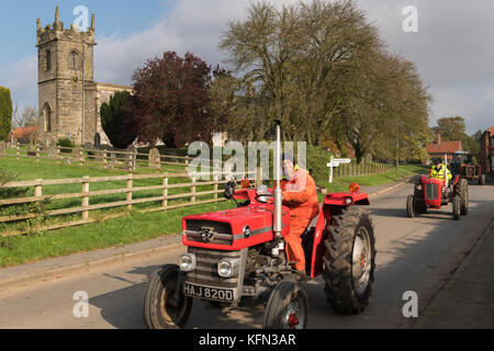 Man driving old red vintage MF tractor through village of Bugthorpe on Wolds Vintage Group Road Run, an annual charity event - Yorkshire, England, UK. Stock Photo