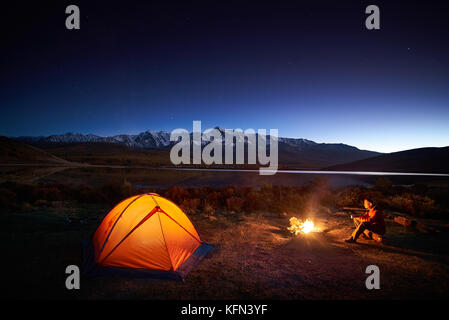 Man tourists sitting in the illuminated tent near campfire Stock Photo