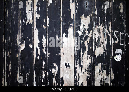 Vandalised, cracked and black peeling paint on boarded up wood windows creates a grunge texture background Stock Photo