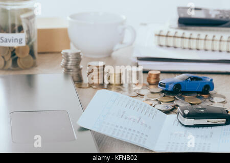 Car insurance and loan concept:Car Key on book bank on desk with Money saving in jar coin bank ,warm tone filter Stock Photo