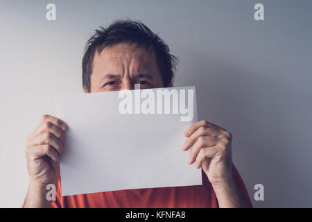 Man hiding behind blank white paper as copy space for text message Stock Photo