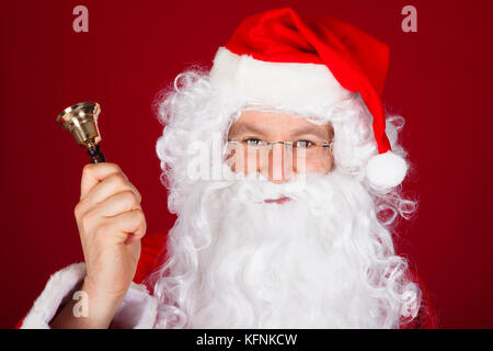Close-up of santa holding bell over red background Stock Photo