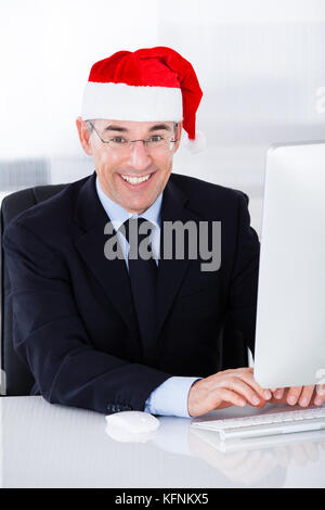 Mature Businessman Wearing Santa Hat Working On Computer In Office Stock Photo
