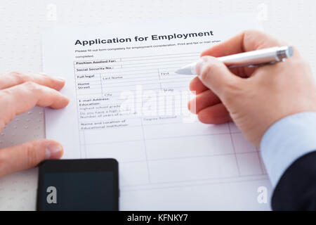 Close-up Of Hand Holding Pen Over Employment Application With Mobile Phone Stock Photo