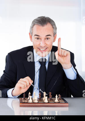 Mature businessman playing chess and gesturing indoors Stock Photo