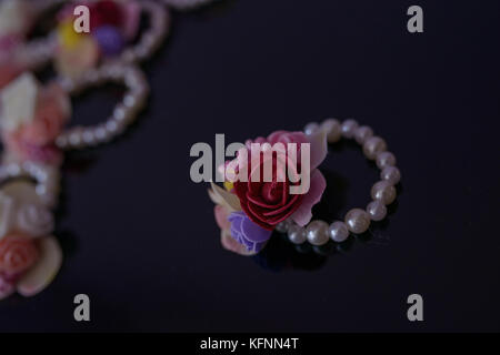 Playful pearl beads bracelet with leather and plastic floral ornaments, on a dark surface with selective focus Stock Photo