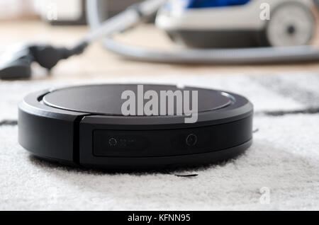 Robotic vacuum cleaner working on carpet. Traditional vacuum cleaner in background Stock Photo