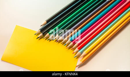 Colored Pencils isolated on white backdrop and blank Yellow note, placed in arc row Stock Photo