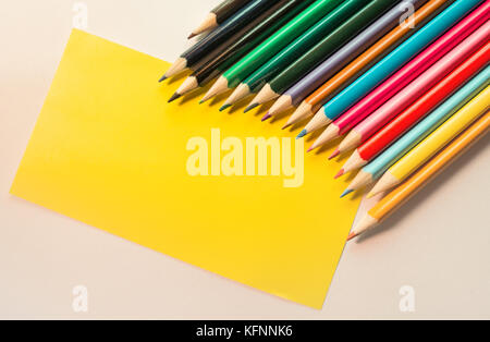 Colored Pencils isolated on white backdrop and blank Yellow note, placed in arc row Stock Photo