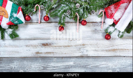 Snowy Christmas fir branches with traditional hats, red ball ornaments and pine cones on rustic wood in flat lay format Stock Photo
