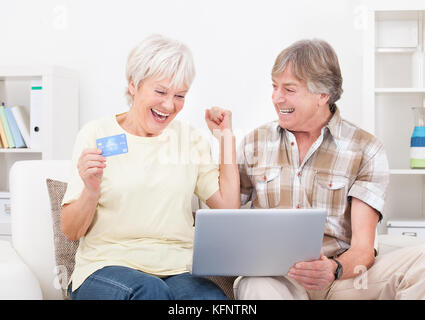 Happy Senior Couple Shopping Online Using Laptop With Credit Card Stock Photo
