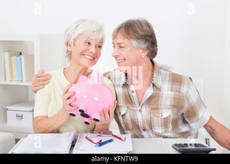Portrait Of Smiling Senior Couple Saving Money In The Pink Piggybank Stock Photo