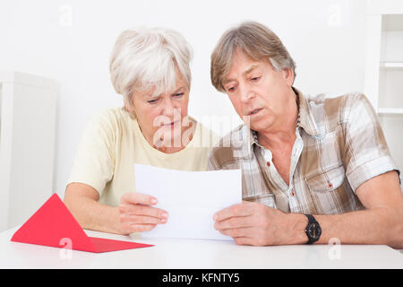 Senior Couple Were Disappointed While Reading Letter On Table Stock Photo