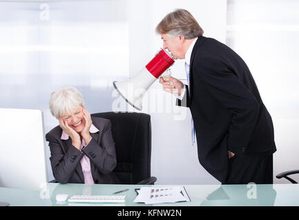 Mature Businessman Yelling At His Coworker With Megaphone At Work Stock Photo