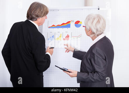 Mature Businessman And Businesswoman Discussing About Graph Shown On Flipchart Stock Photo