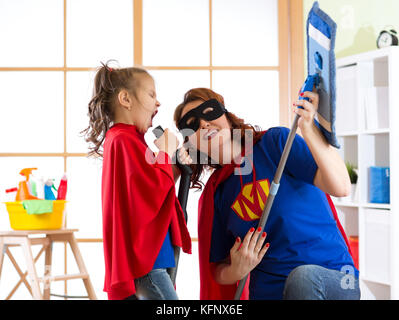 Cleaning concept. Super hero woman and daughter playing guitar and singing on cleaning equipment. Family ready to cleaning. Stock Photo