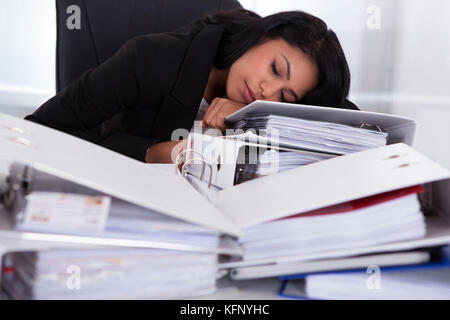Young Businesswoman Sleeping On Piles Of Folders In Office Stock Photo