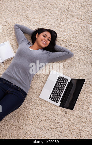 Top View Of Young Woman Lying On Carpet With Laptop Stock Photo