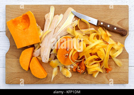 Cut up butternut squash with peels and knife on brown wood chopping board isolated on white from above. Stock Photo