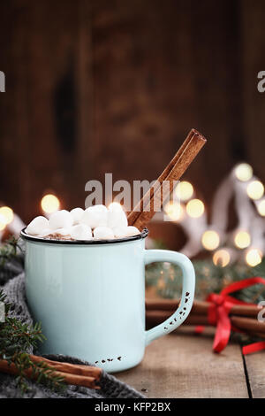 Enamel cup of hot cocoa with mini marshmallows and cinnamon bark.  Pine boughs and gray scarf against a rustic background with beautiful Christmas lig Stock Photo