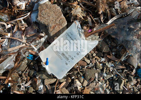 A medical hospital saline drip bag intact washed up with other plastic items on a pebble beach in Menorca Spain Stock Photo