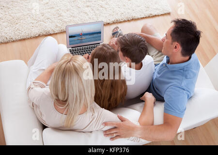 A Happy Family With Two Children Sitting On A Sofa Using Laptop At Home Stock Photo