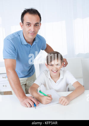 Portrait Of A Boy Doing Homework With His Father At Home Stock Photo