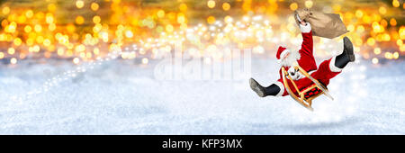 crazy santa claus flying on his sleigh with bag of presents in front of snowy  bright golden lights bokeh wide panorama background Stock Photo