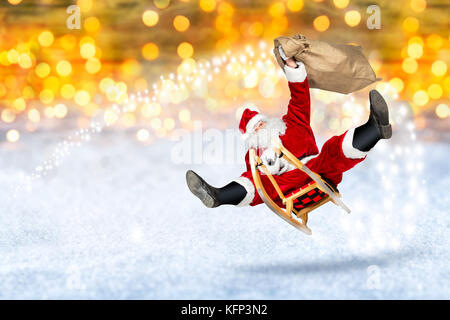 crazy santa claus flying on his sleigh with bag of presents in front of snowy  bright golden lights bokeh background Stock Photo