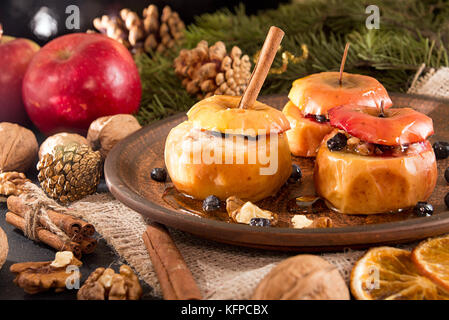 Baked apples on brown plate with holiday Christmas decoration with Christmas tree branch, cones, cinnamon, walnuts and red apple. Stock Photo