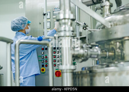 Female worker at pharmaceutical factory operating control panel of the pharmaceutical machine. Stock Photo