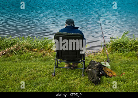 elder fisherman sitting on the riverbank and waiting to catch a fish Stock Photo